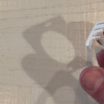 Close-up of a hand holding a white lanyard clip with a shadow on a wooden surface.