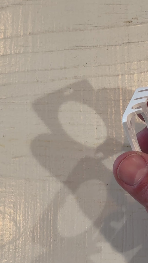 Close-up of a hand holding a white lanyard clip with a shadow on a wooden surface.